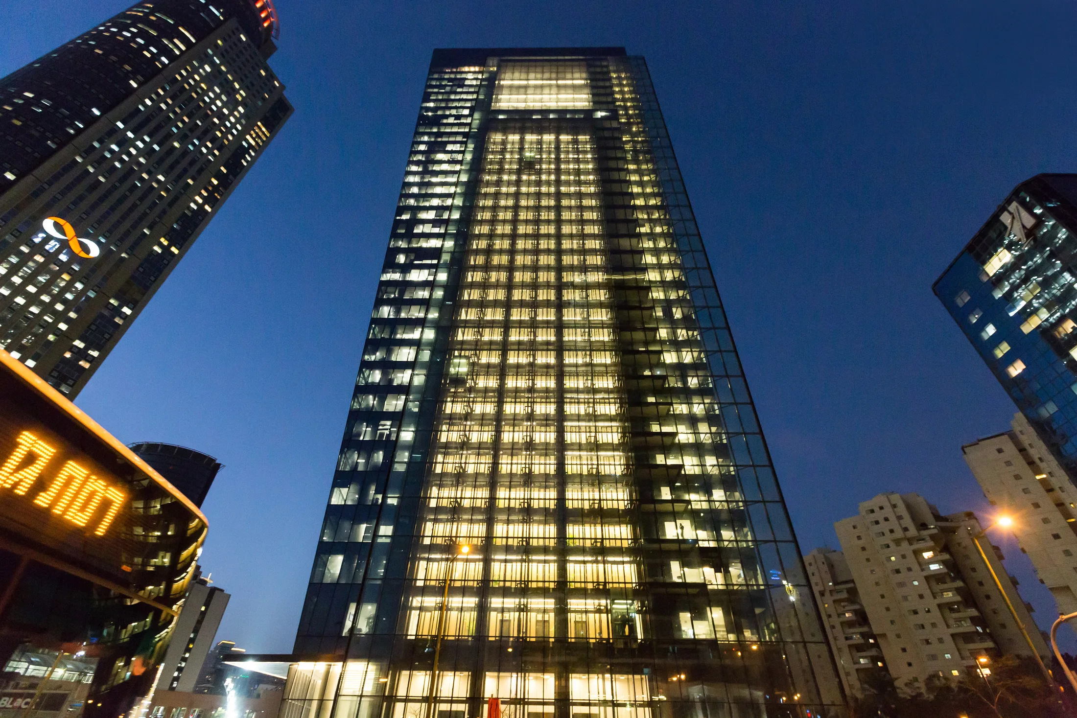The tower and its lit base among neighboring high-rises